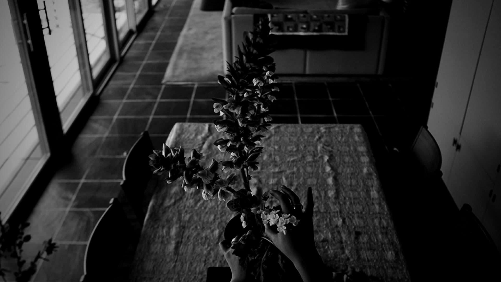 Florist Amanda Luu shaping a tall ikebana arrangement over a dining table, seen from above