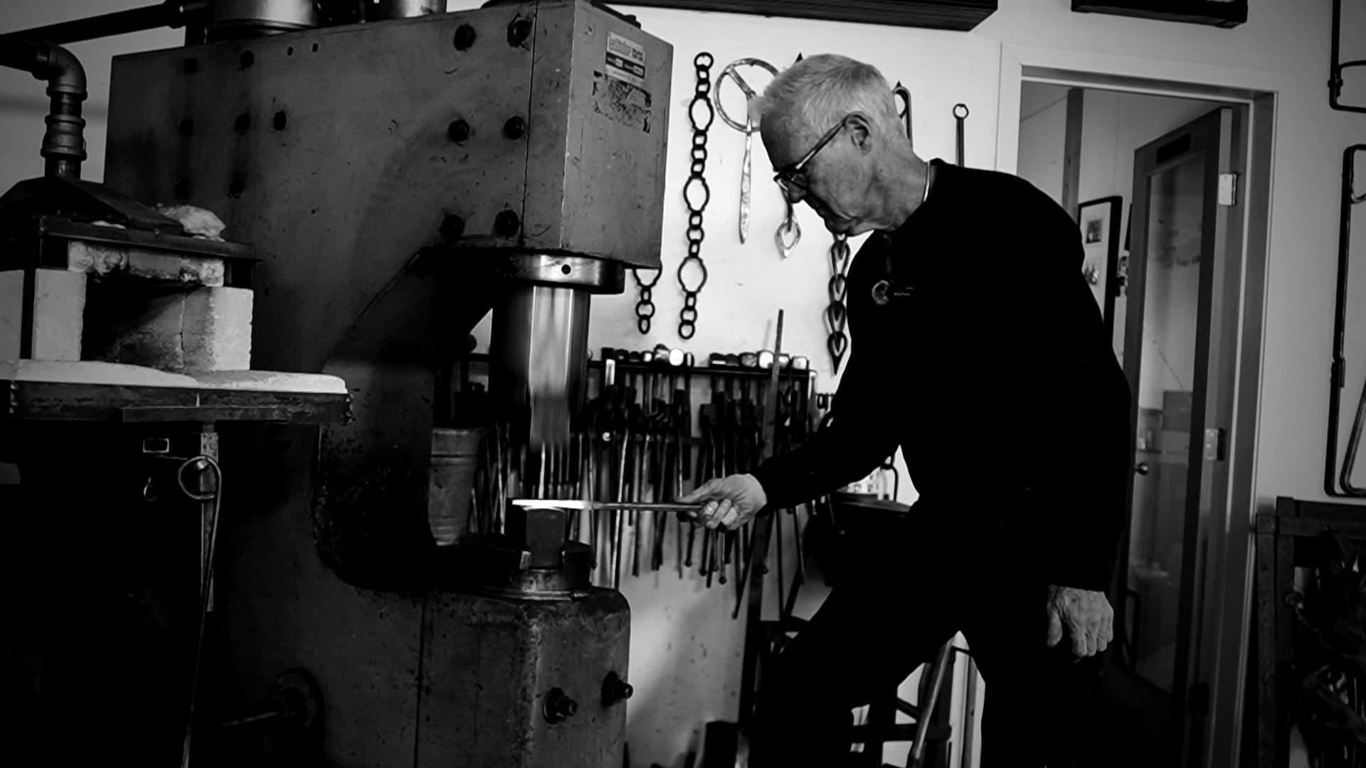 Architectural blacksmith Jefferson Mack at the forge, holding hot iron to the power hammer