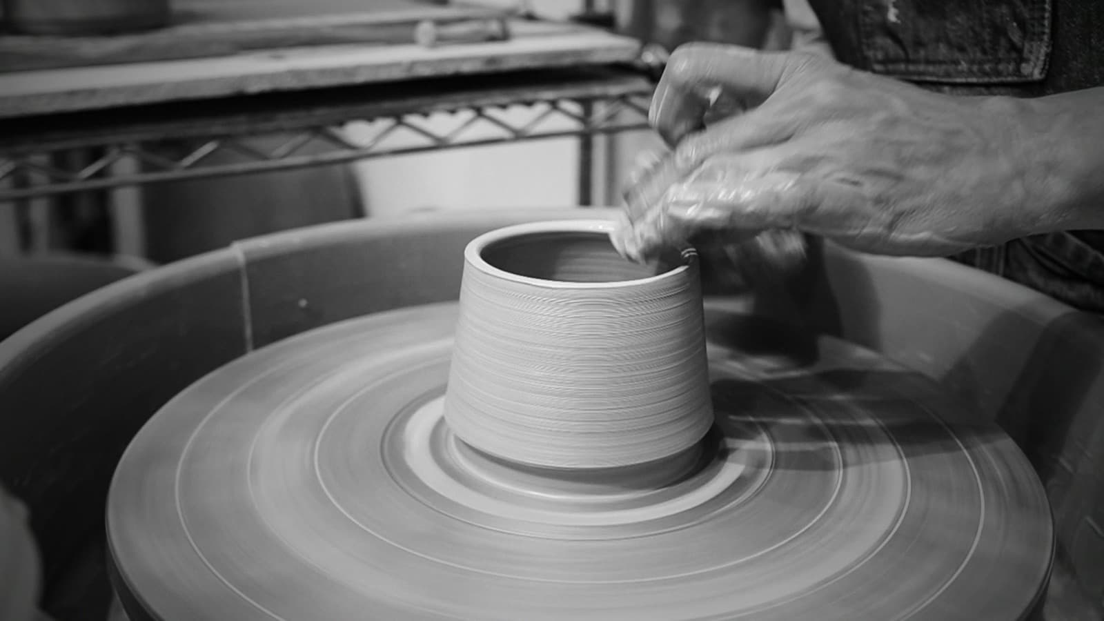 A potter's hands draw up the wall of a cylinder spinning on the wheel.