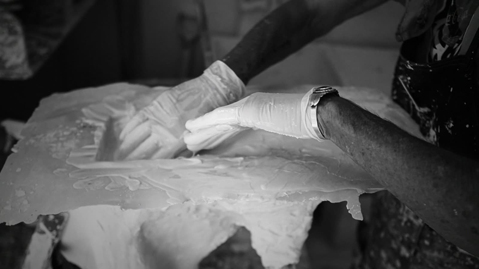 Gloved hands spread and smooth wet plaster across a mold in an ornamental plaster workshop.